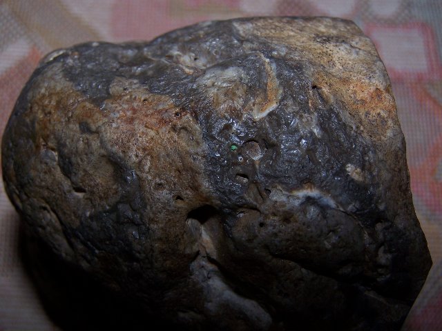Dieses Bild zeigt die Seitenansicht des Meteoriten nach den Abschlägen zur Findung der Fossilien und Abschnitten für die chemische Probe. Er zeigt unterschiedliche Brandspuren,die aus dem unterschiedlichen Material der Kruste, 
Opal und Chacedon, bestehen. In der Mitte ist punktartig ein grünes Material zu sehen, das auch im Inneren des Meteoriten vorhanden war.
